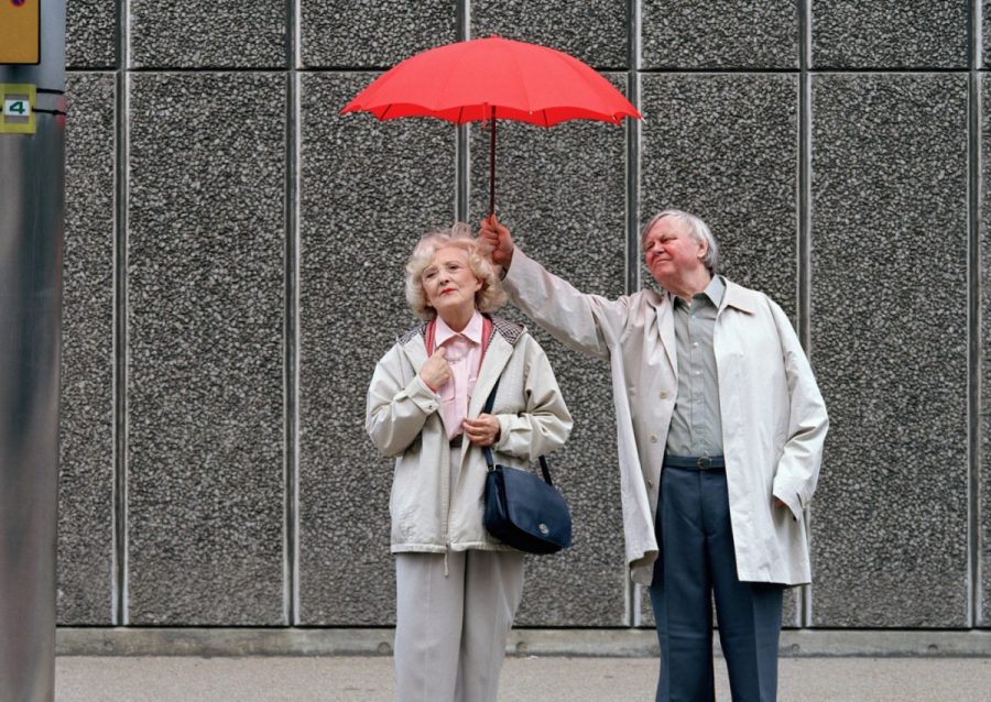 Senior man holding red umbrella over woman, standing on pavement